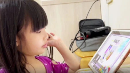 小女孩坐在書桌前專心看著平板上的英文課